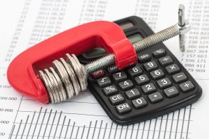 Featured image that includes a calculator, a spreadsheet and coins held by a clamp.